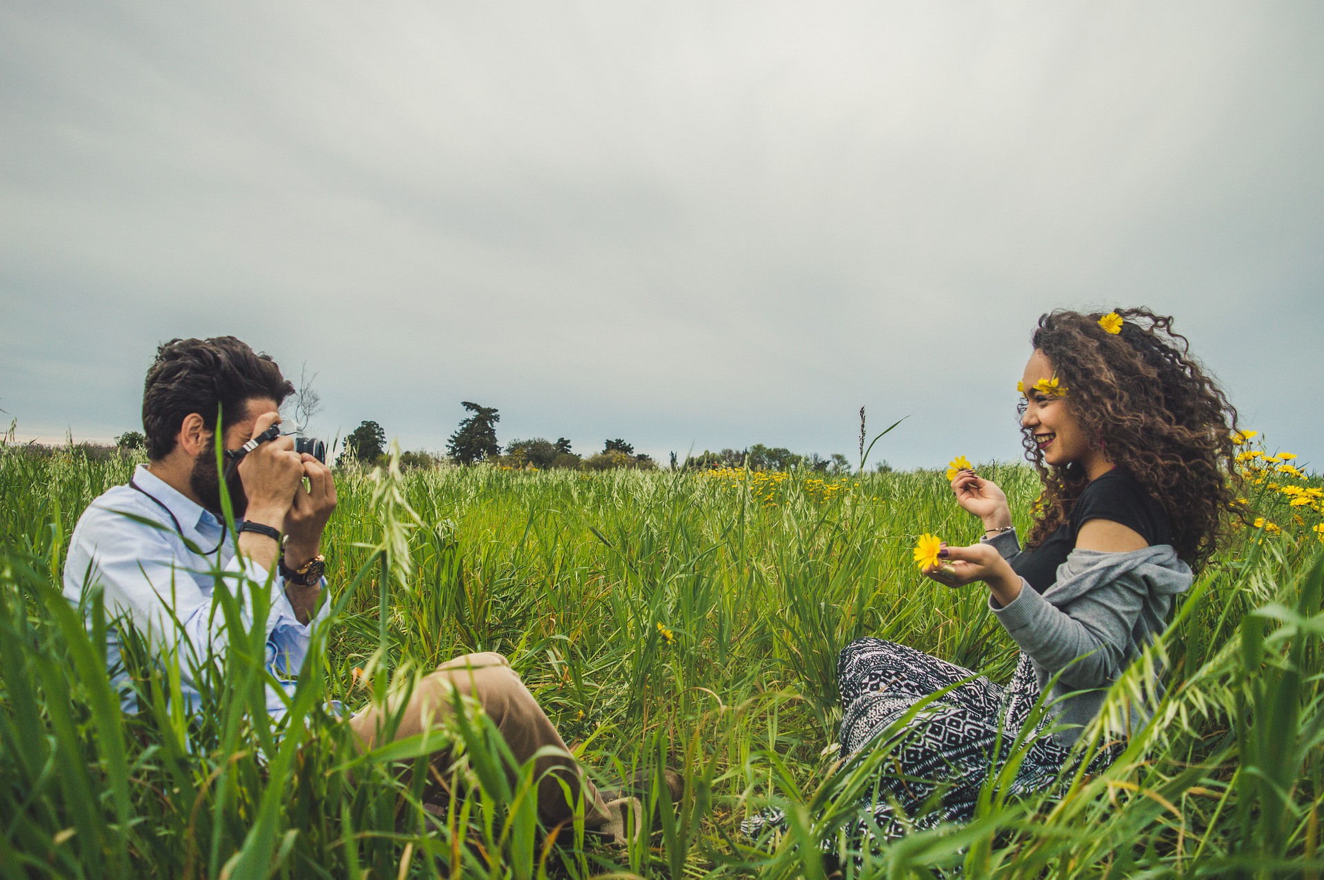Novio sacándole una foto a su novia sentados en el campo